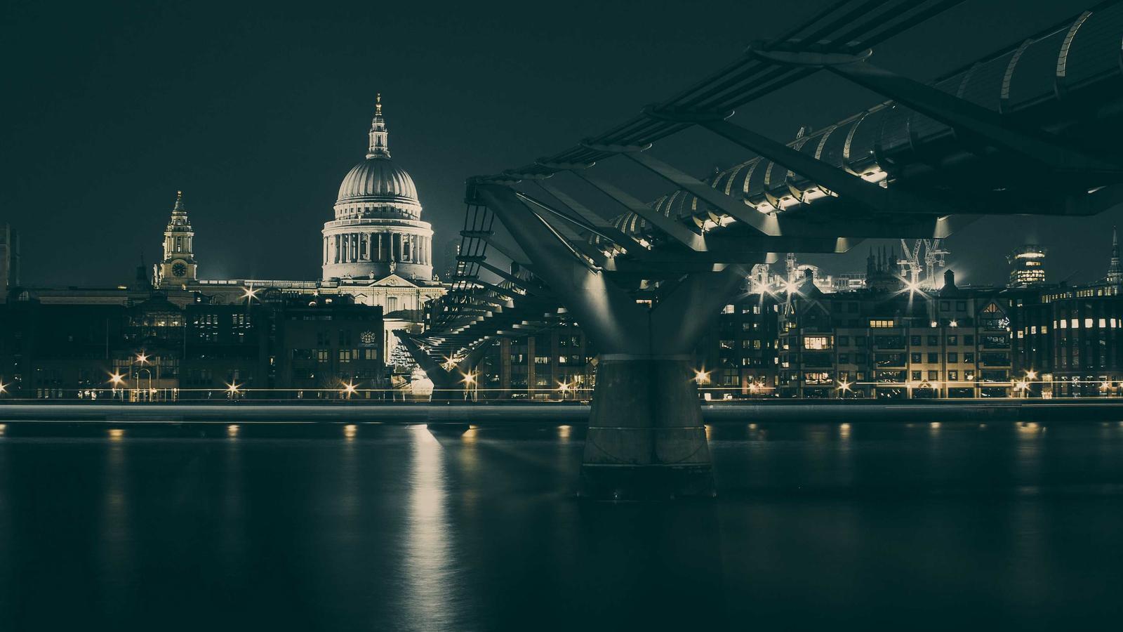 A domed cathedral and a footbridge lit above a river at night